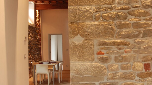 Un arco de piedra que da acceso a un comedor con piso de madera y pared de piedra.