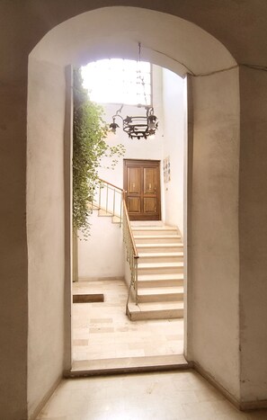 A hallway with a wooden staircase, a door at the bottom, and a hanging light fixture.