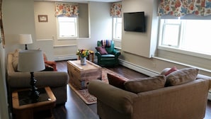 Un salon comprenant un canapé, un fauteuil, une table basse, une lampe et un téléviseur à écran plat fixé au mur.