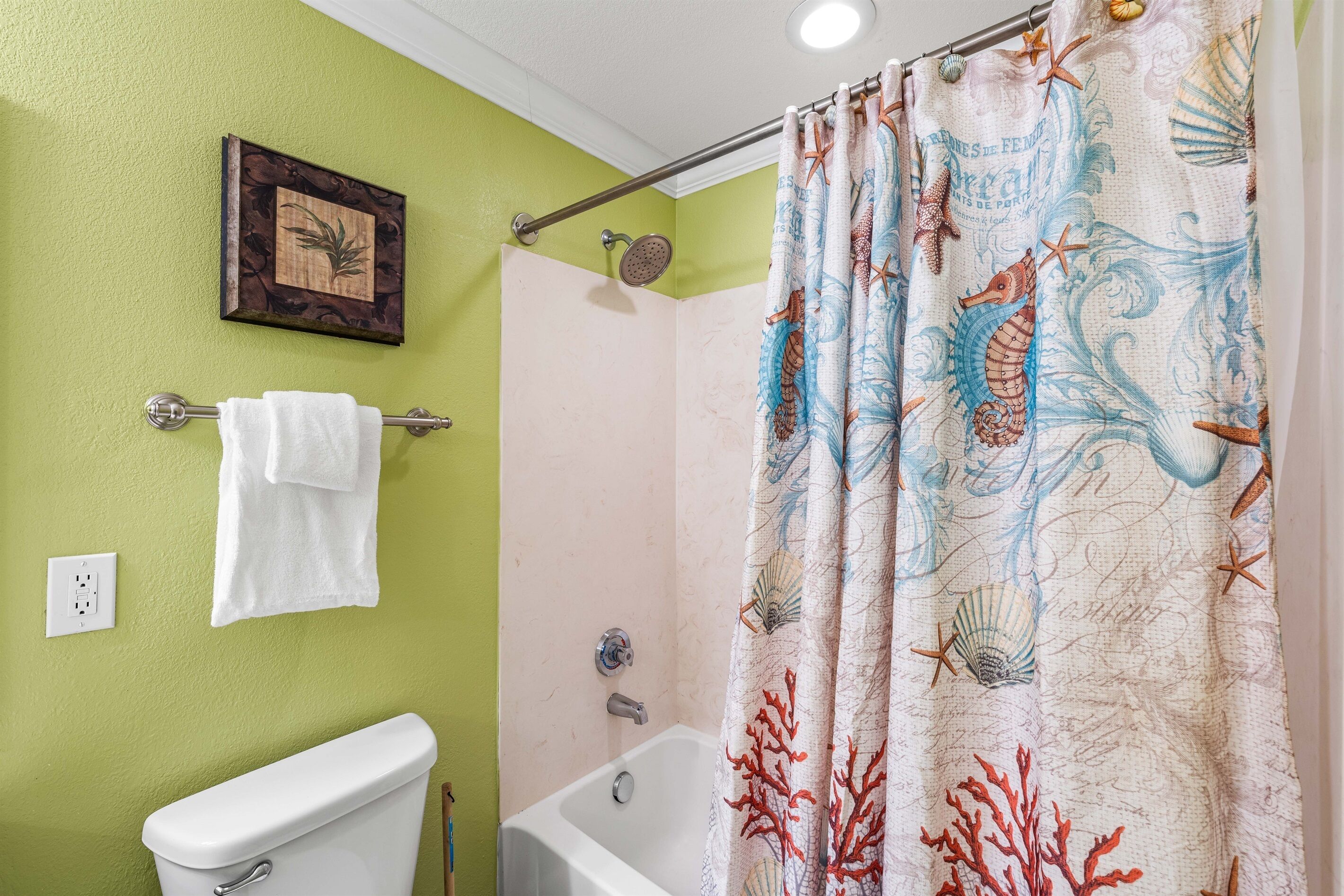 Un baño con pared verde, inodoro blanco, bañera y cortina de ducha con motivos de criaturas marinas.