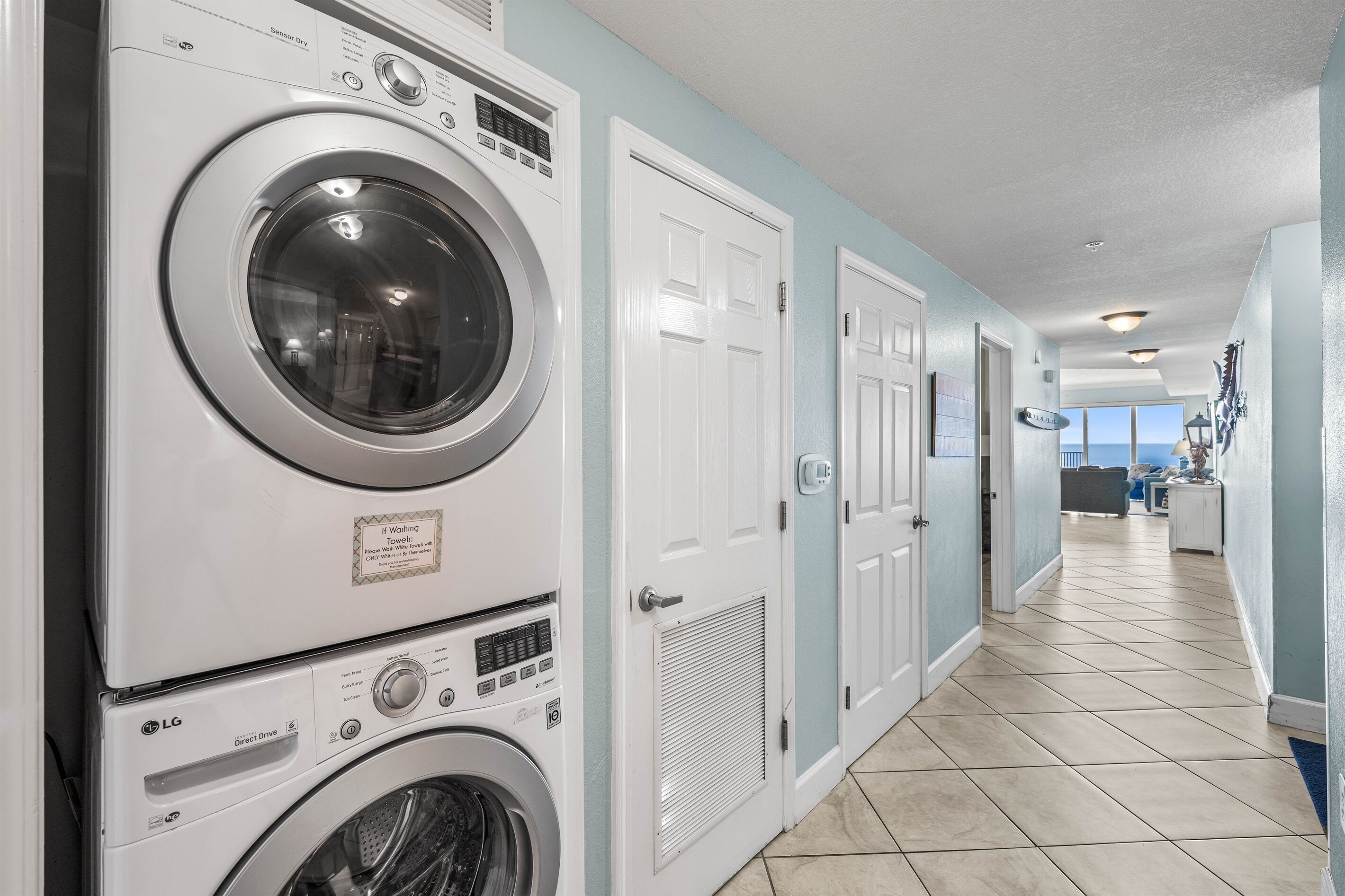 A laundry room with stacked washers and dryers, a tiled floor, and a view of the ocean through a door.