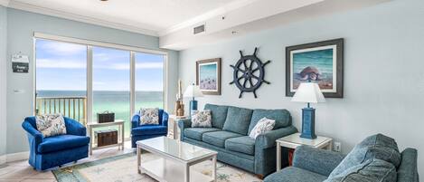 A living room with a view of the ocean, a ceiling fan, and nautical-themed decor.