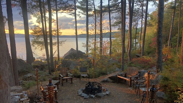 Un espace boisé avec un foyer, des sièges et une vue sur un lac au coucher du soleil.