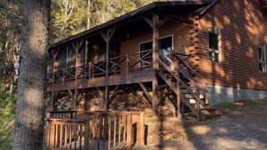 Une cabane en rondins dotée d’une terrasse en bois et d’un escalier menant à un porche.
