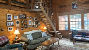 L’intérieur d’un chalet accueillant, avec un escalier en bois, un canapé recouvert d’une couverture, une table basse et un tapis.