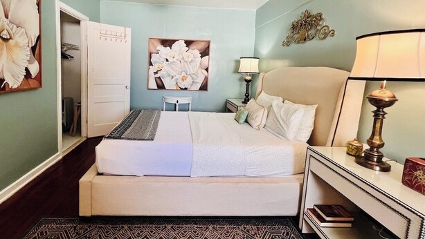 A bedroom with a bed, a ceiling fan, a nightstand with a lamp, a mirror, and a wall decoration. - One Bedroom Apartment #3 in Historic Burns Square district, downtown Sarasota (Sarasota)