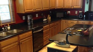 A kitchen with wooden cabinets, a black countertop, a stove, and a sink. - Lakefront Cabin: Private Water Access, Boat Parking, Lake View & Wi-Fi (Burnside)