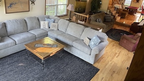 A living room with a grey sectional sofa, a wooden coffee table, and a black rug. There is a painting on the wall and a star decoration. - Lakefront Cabin: Private Water Access, Boat Parking, Lake View & Wi-Fi (Burnside)