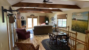 A spacious living area with a wooden ceiling, a dining table with chairs, a sofa, and a television. - Lakefront Cabin: Private Water Access, Boat Parking, Lake View & Wi-Fi (Burnside)