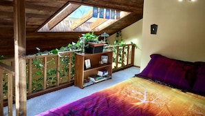 A cozy attic bedroom with a sloped ceiling, wooden beams, a skylight, a bed with a colorful blanket, a small bookshelf, and a potted plant. - Gorgeous Pacific Northwest Private Lodge in Southeast Eugene (Eugene)