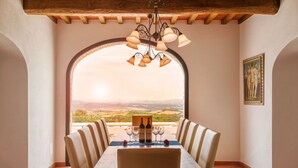 A dining area with a table set for two, a chandelier, and a view of the countryside. - ISOLA SERENA Newly Expanded Private Luxury Villa, Tuscany, Infinity Pool & Views (Castellina in Chianti)