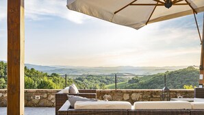 A wicker outdoor seating area with a stone wall backdrop and a scenic view of rolling hills. - ISOLA SERENA Newly Expanded Private Luxury Villa, Tuscany, Infinity Pool & Views (Castellina in Chianti)