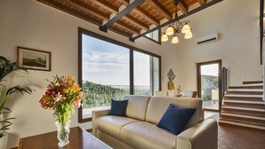 A spacious living room with a beige sofa, a wooden coffee table, and a vase of flowers. Large windows provide a view of the outdoors. - ISOLA SERENA Newly Expanded Private Luxury Villa, Tuscany, Infinity Pool & Views (Castellina in Chianti)