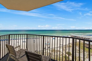 A balcony with a view of a beach, equipped with chairs and a table.