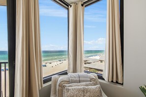 Une chambre avec vue sur la plage, comprenant une fenêtre avec des rideaux, un lit avec une couverture et un oreiller.