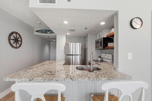 A kitchen with a granite countertop, stainless steel appliances, and white bar stools. - Beautiful One Bedroom Ocean Front Condo with a Free Beach Chair/Umbrella set up! (Panama City)