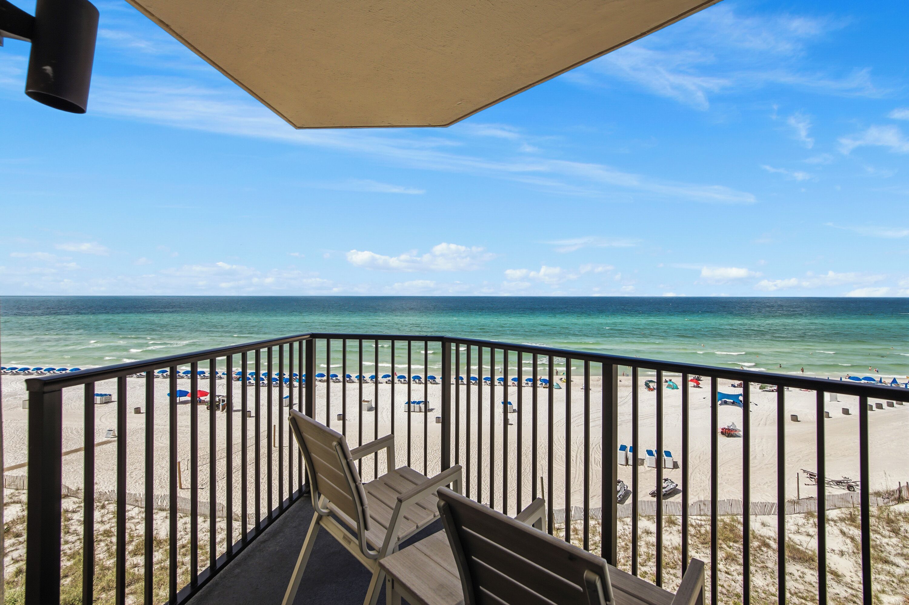 A beach view from a balcony with a railing, a table, and chairs.