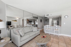 A modern living room with a grey sofa, a coffee table, and a kitchen area with a fridge, microwave, and cabinets. - Beautiful One Bedroom Ocean Front Condo with a Free Beach Chair/Umbrella set up! (Panama City)