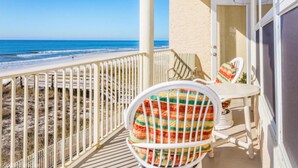 Un balcone con vista sulla spiaggia e sull'oceano. Si nota una sedia bianca con un cuscino colorato e un tavolo con una sedia bianca.