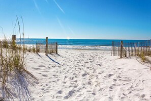 A sandy beach path leading to the ocean, with a wooden fence on the left and right sides.