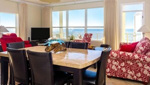Camera d'hotel con zona pranzo, televisione, ventilatore a soffitto e vista sull'oceano.