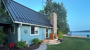 Una casa con chimenea de piedra, terraza y vista al agua.