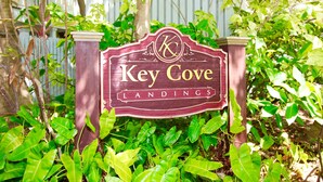 En träskylt med texten ”Key Cove Landings”, omgiven av frodigt, grönt lövverk.