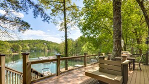 A wooden deck with a bench and railing overlooking a lake with boats, surrounded by trees. - Lake Front, PETS, Theater, Dock, Swim-Fish-Boat,  Fire Pit, NEW BOAT, Pickleball (Waleska)
