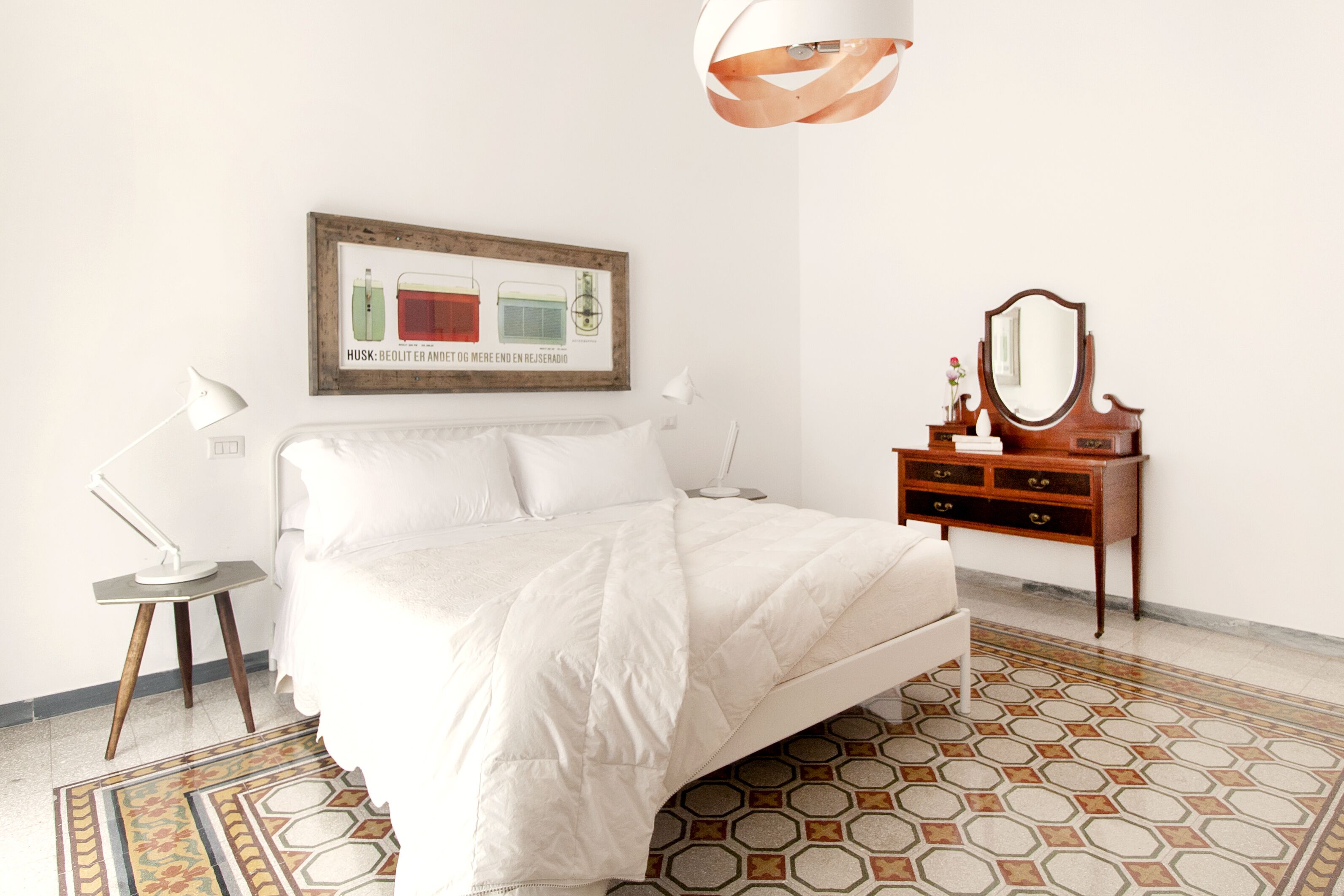 A neatly arranged bedroom with a bed, bedside lamp, dresser, mirror, and a framed picture on the wall.