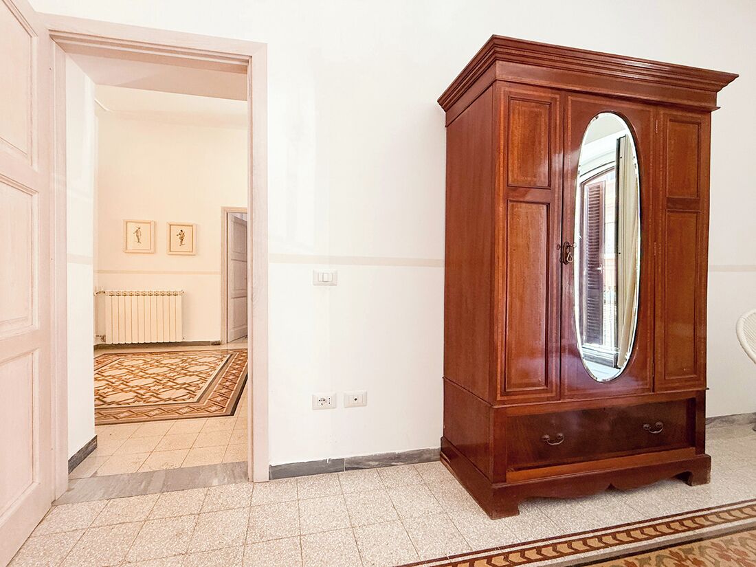A wooden armoire with a large mirror, a patterned rug, and a radiator in the background.