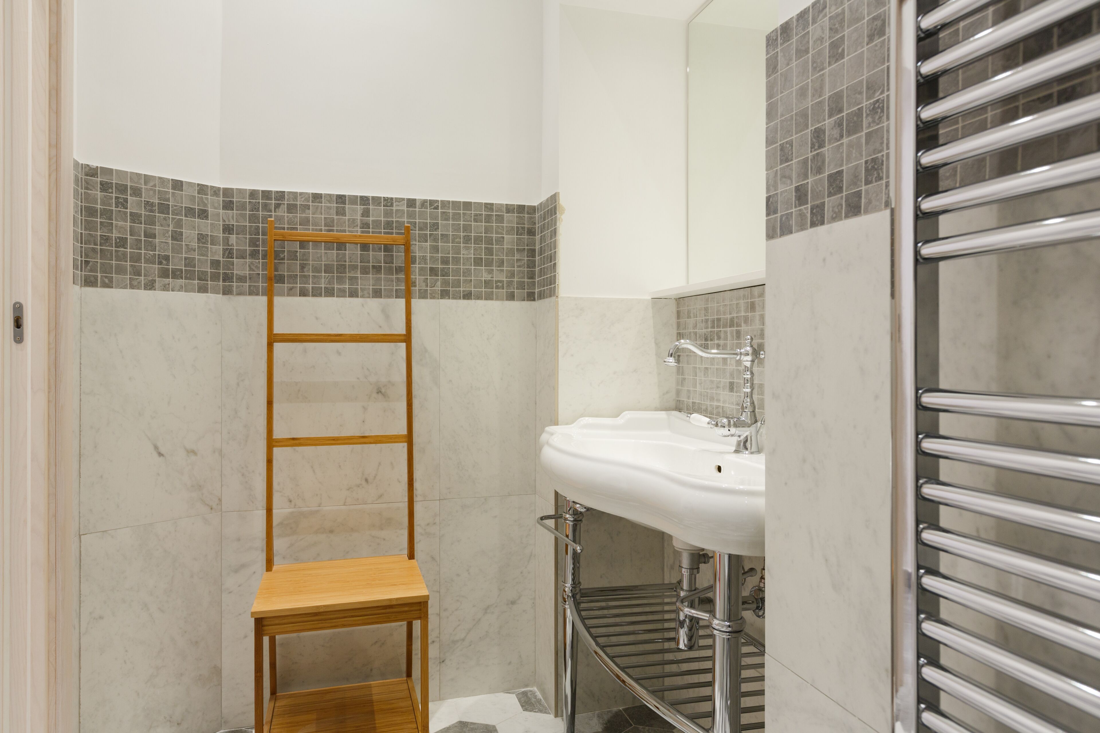 A bathroom with a wooden shelf, a white sink, and a tiled shower area.