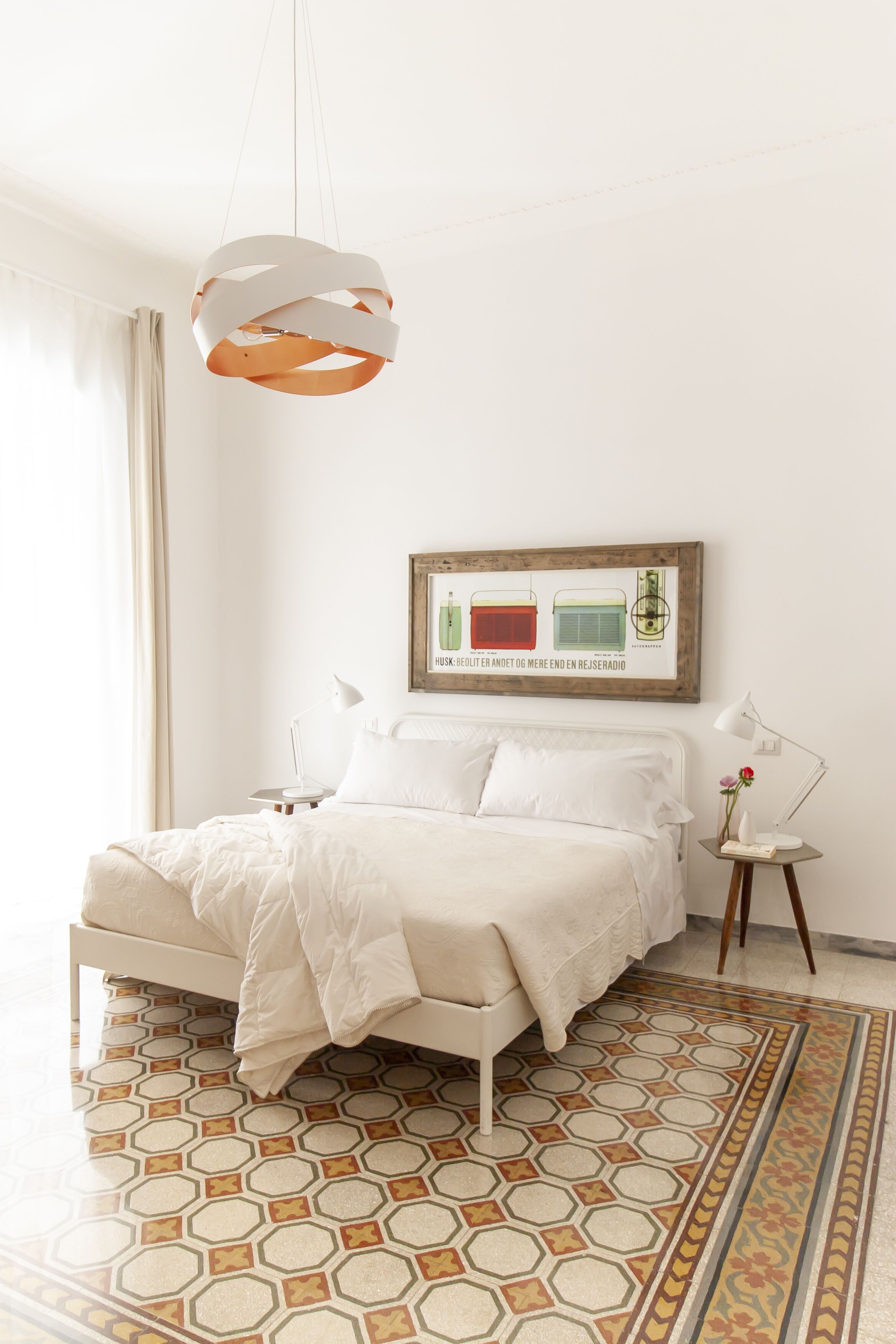 A modern bedroom with a bed, a hanging light fixture, a bedside table with a lamp, and a framed picture on the wall.