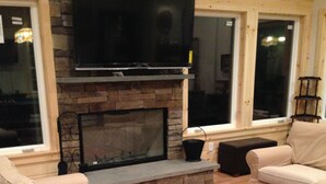 Una sala de estar acogedora con chimenea de piedra, sofás color beige y un televisor de pantalla plana montado encima.