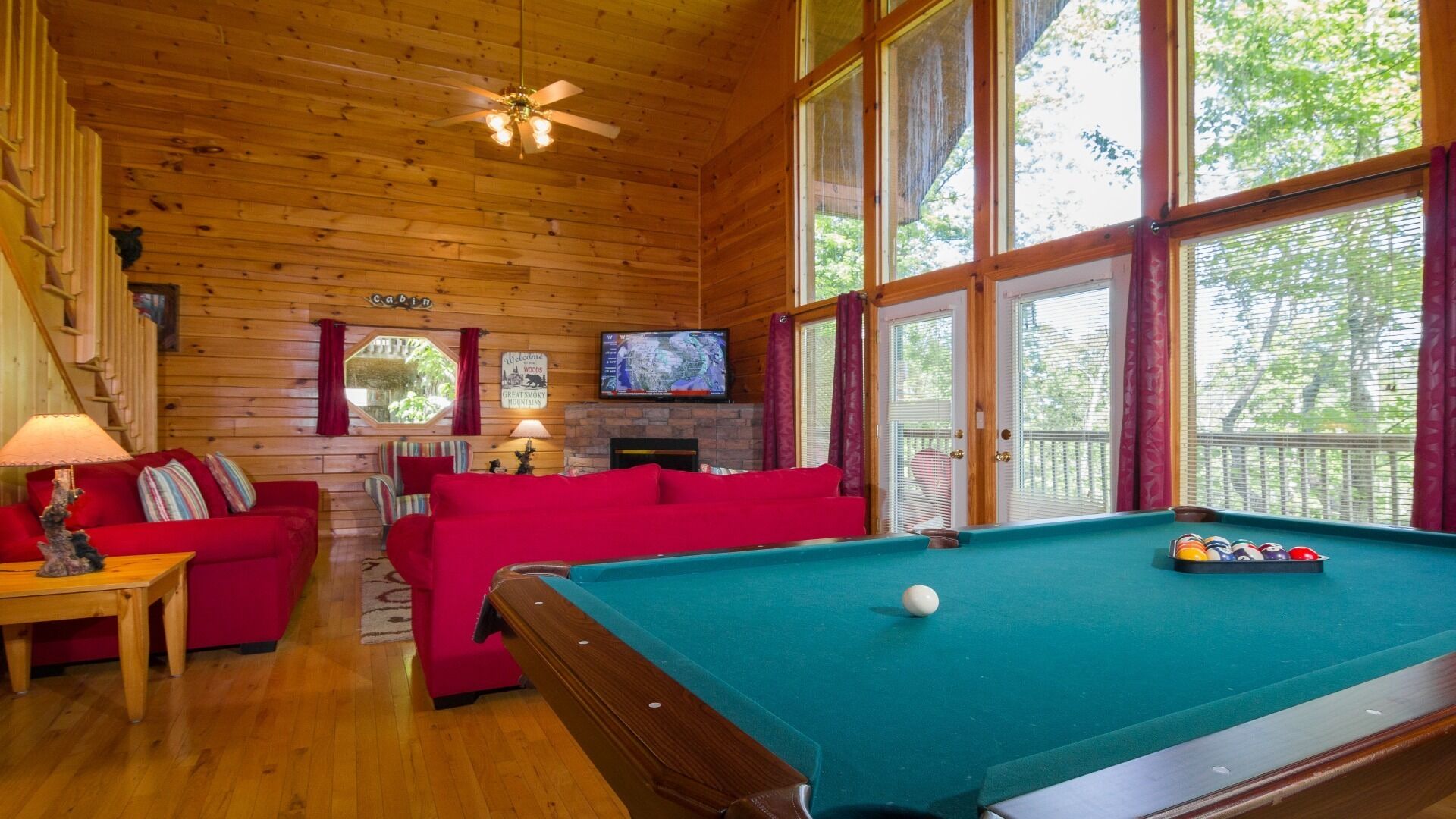 A cabin interior with a pool table, red sofas, a television, and a fireplace.