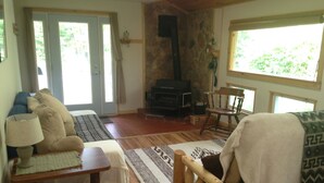 Uma sala de estar acolhedora com sofá, mesa de madeira, lareira e vista para o verde pelas janelas.