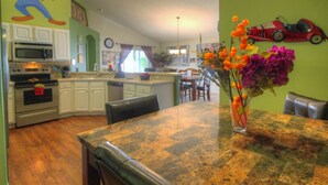 A kitchen with white cabinets, a microwave, and a stove. There is a dining table with chairs and a vase of flowers.