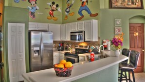 A kitchen with Mickey Mouse and Donald Duck murals, stainless steel appliances, and a fruit basket on the counter.