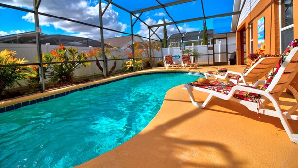 An indoor swimming pool with clear blue water, surrounded by a glass enclosure, and equipped with lounge chairs and a sunshade.