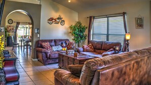 A spacious living room with a brown leather sofa, a coffee table, and a dining area with a table and chairs.