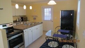 A compact kitchen with white cabinets, a black stove, a microwave, and a refrigerator. There is a small dining area with a table and chairs. - Downtown South Haven, close to everything,  family friendly, very clean (South Haven)