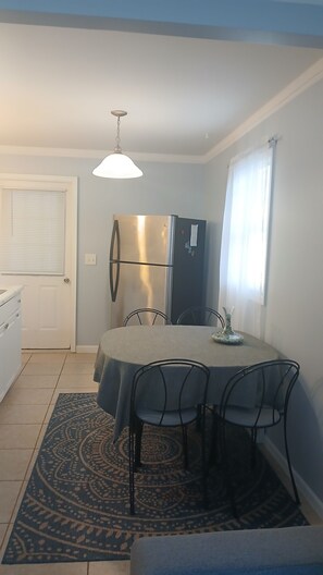 A compact dining area with a table and chairs, a refrigerator, and a patterned rug.