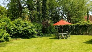 A well-maintained lawn with a table and chairs under a red umbrella, surrounded by dense greenery. - Downtown South Haven, close to everything,  family friendly, very clean (South Haven)