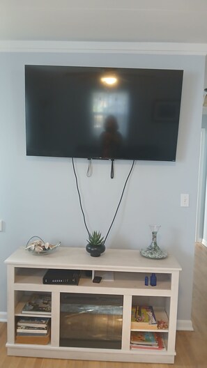A flat-screen TV mounted on a wall above a white entertainment center with shelves, a small plant, and decorative items.