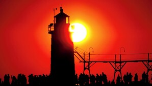 A silhouette of a tall tower with a balcony, set against a sunset with a bright sun.
