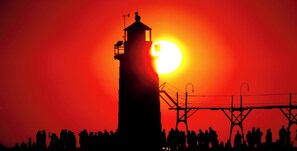 A silhouette of a tall tower with a balcony, set against a sunset with a bright sun.