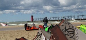 Ein Strand mit Windsurfgeräten und einem Leuchtturm im Hintergrund.