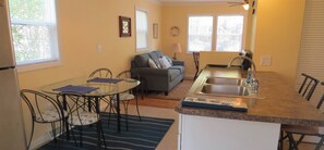 Cozy living space with a kitchenette and seating area, featuring a sofa, table, chairs, sink, and stove.