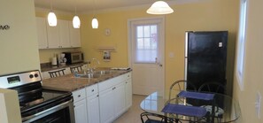 A compact kitchen with white cabinets, a black stove, a microwave, and a refrigerator. There is a small dining area with a table and chairs.