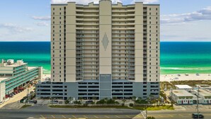 A high-rise hotel with a central atrium and multiple balconies, located near a beach with clear blue waters. - 4th Newest Beachfront Condo! 100% No Smoking (Panama City Beach)