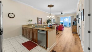 A spacious kitchen with a dishwasher, a red rug, and a view to the living area. - 4th Newest Beachfront Condo! 100% No Smoking (Panama City Beach)